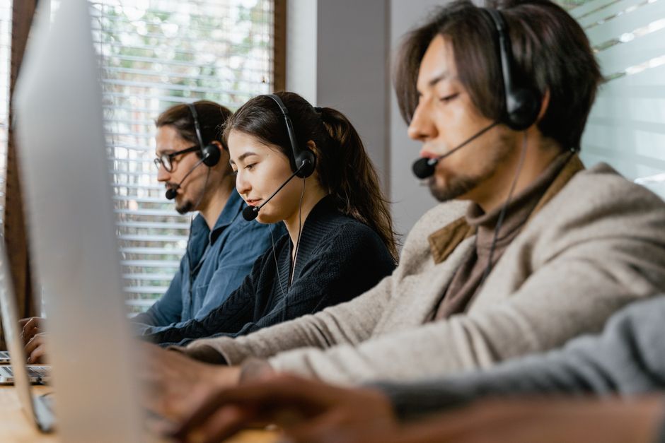 Três agentes de call center trabalhando diligentementemente com fones de ouvido em um ambiente de escritório, demonstrando trabalho em equipe.
