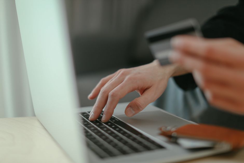 Close-up de mãos segurando um cartão de crédito e digitando em um teclado de laptop para compras online.