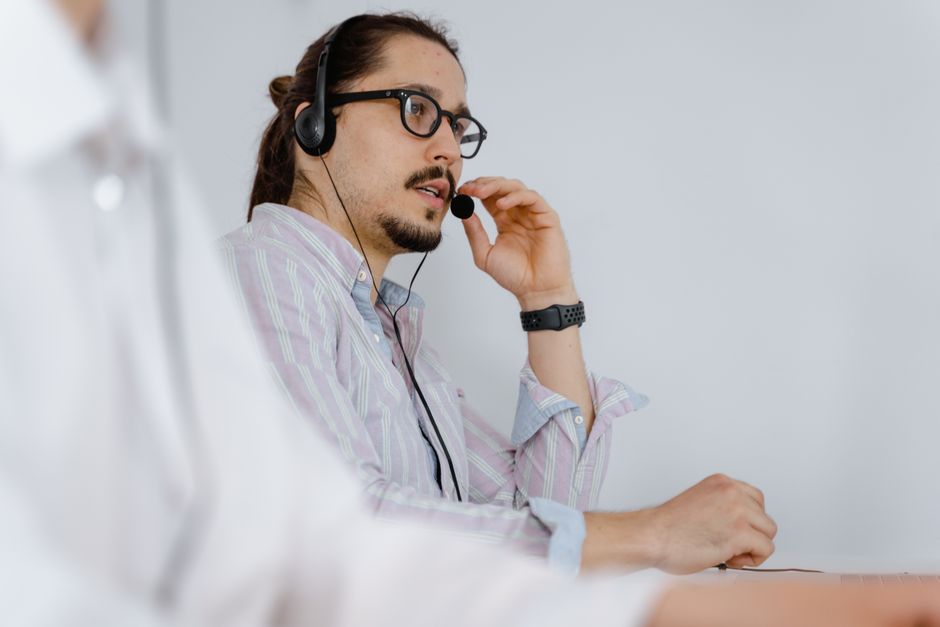 Agente de atendimento ao cliente focado falando com um fone de ouvido em um ambiente de escritório moderno.