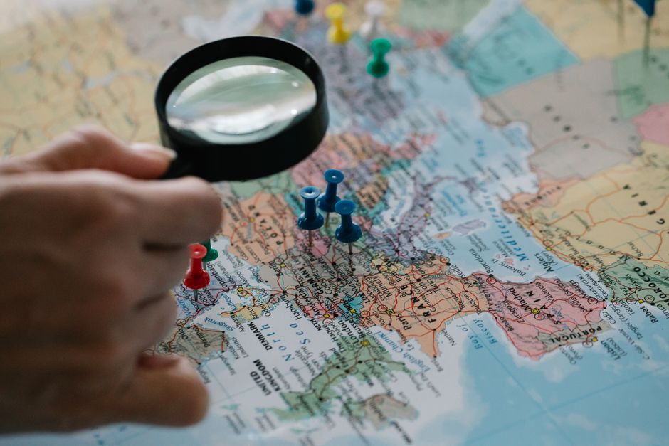 Lupa foca em alfinetes destacando destinos de viagem em um mapa mundi.