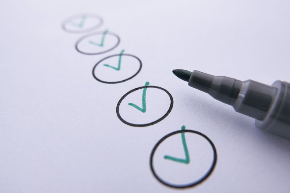 Close-up de uma lista de verificação com marcas de seleção verdes em papel branco usando um marcador.