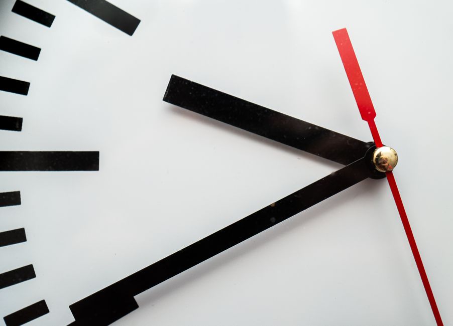 Um close minimalista do mostrador de um relógio de parede, exibindo as horas com ponteiros em negrito nas cores preto e vermelho.