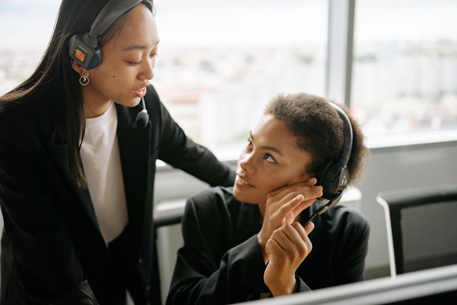 Duas atendentes de call center discutindo estratégias com headsets em um ambiente de escritório moderno.